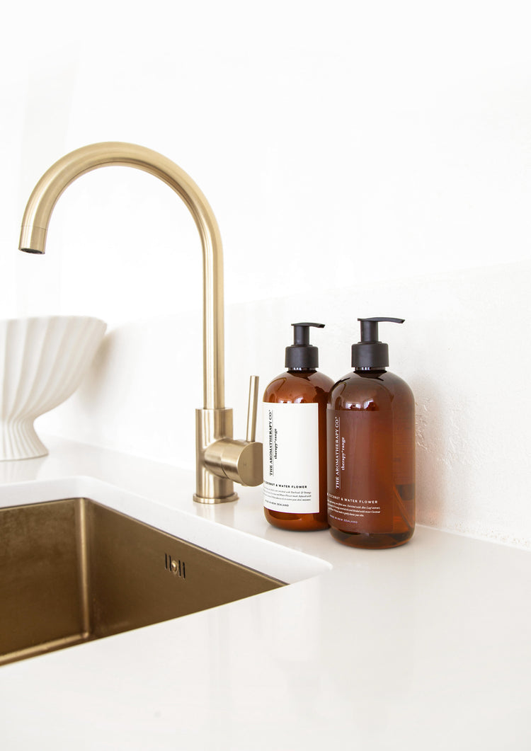 Therapy lotion and wash bottles beside a brass gooseneck tap and brass sink with a fluted bowl