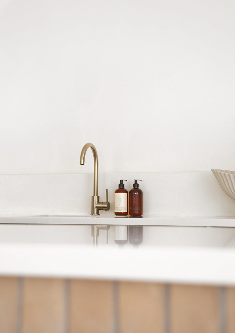 Brass gooseneck tap and two small amber bottles on a white bench above a timber cabinet