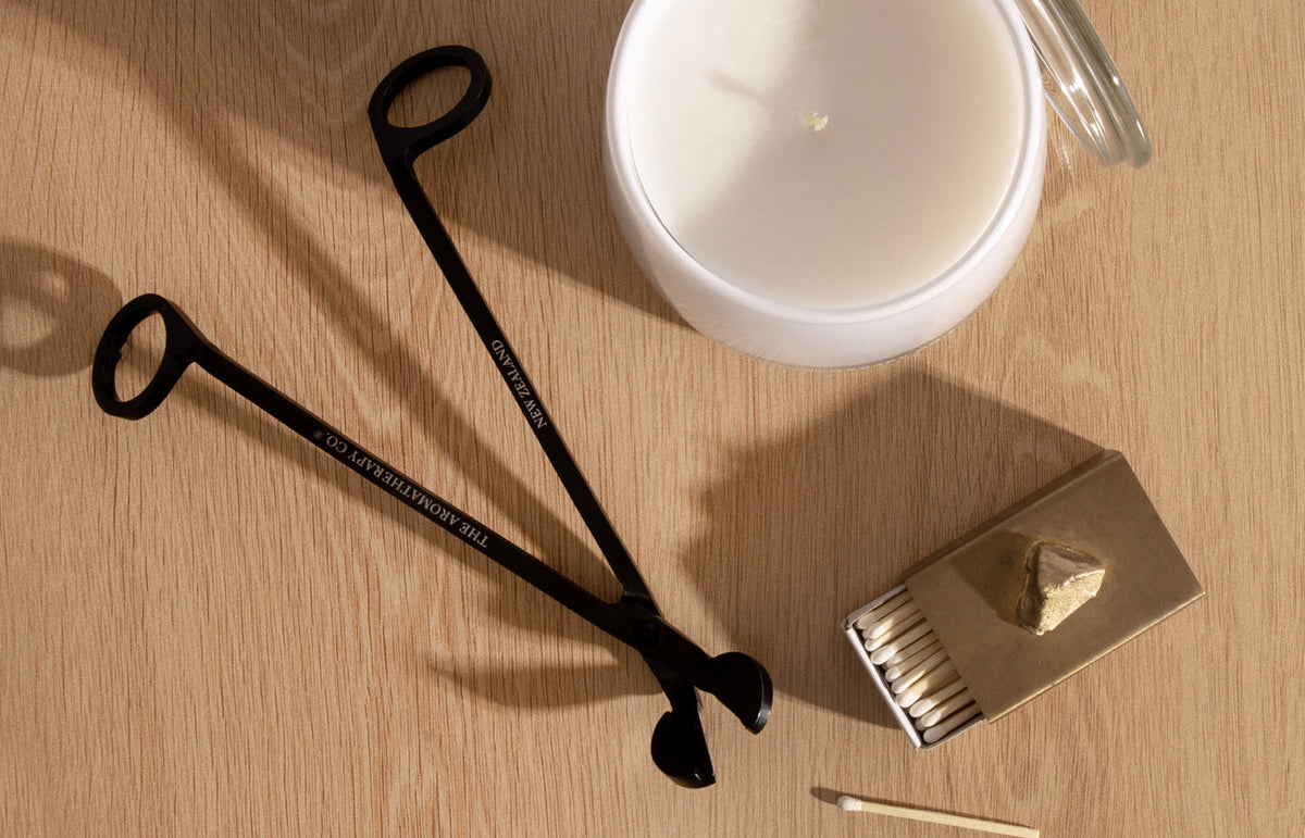 Wick trimmer and candle snuffer beside a Therapy candle on stone