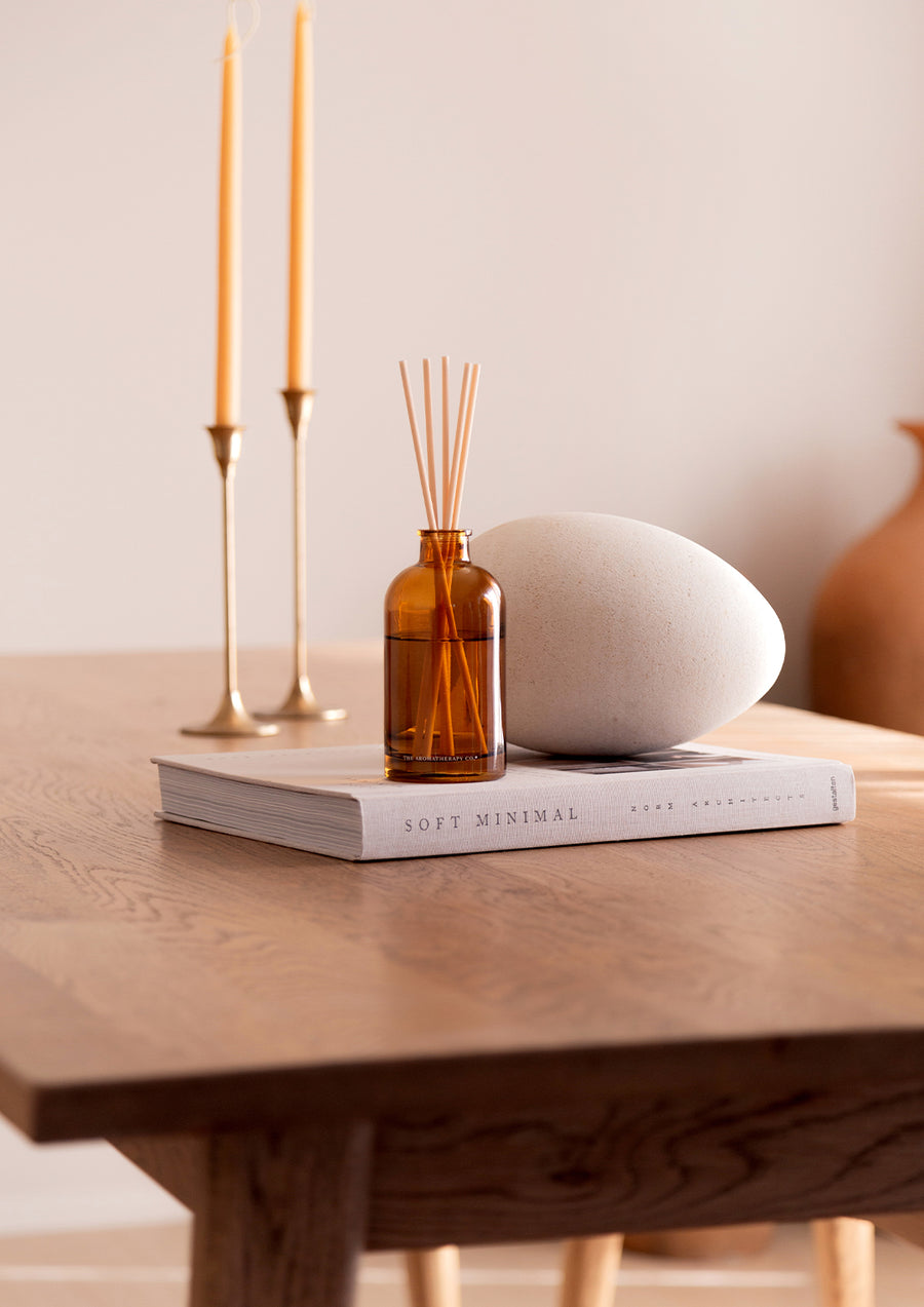Therapy diffuser on a book beside taper candles and a pale stone on a timber table
