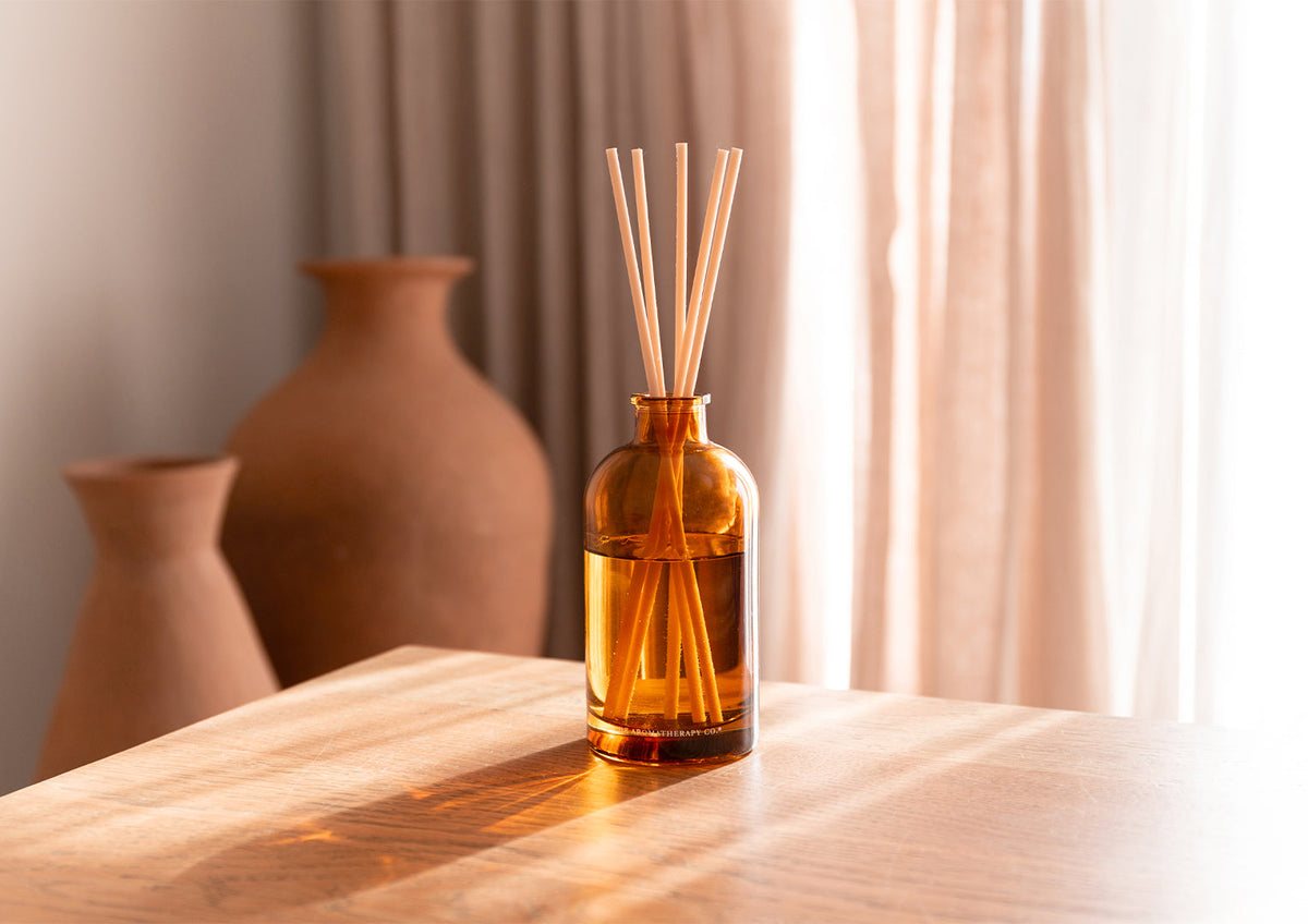Therapy amber diffuser on a timber table with terracotta vases and a sheer curtain