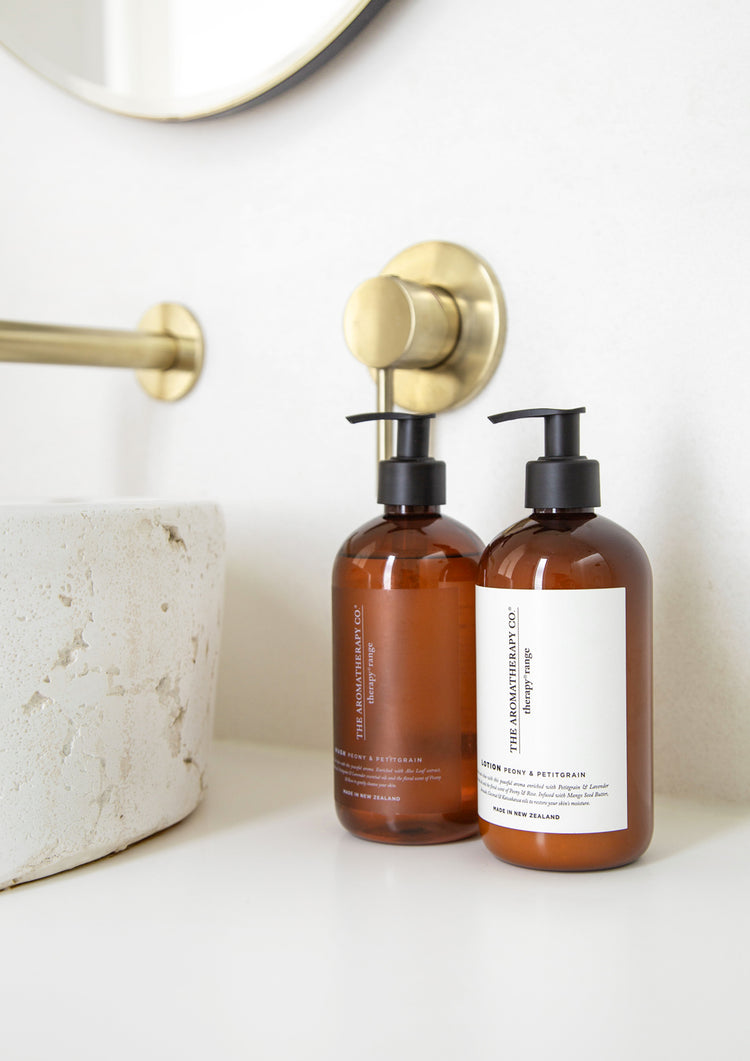Therapy wash and lotion bottles on a white vanity beside a stone basin and brushed brass tapware