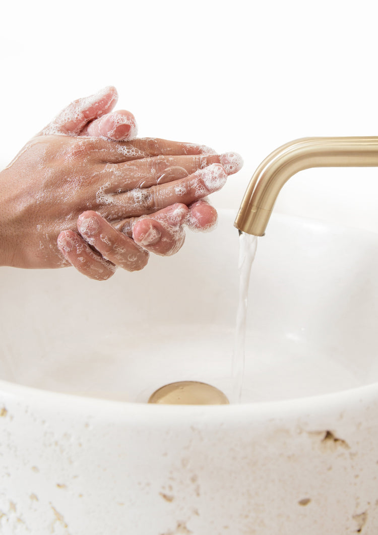 Soapy hands under running water from a brushed brass spout over a white stone basin