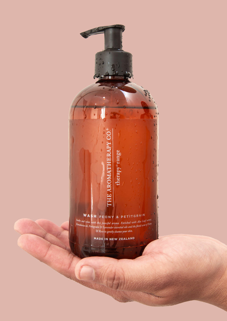 Hand holding the Peony & Petitgrain wash bottle against a dusty pink background