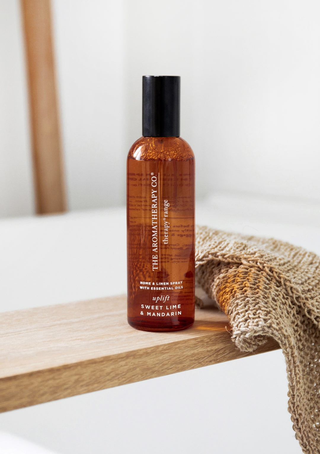 Amber room spray bottle on a timber bath caddy beside a folded woven linen cloth