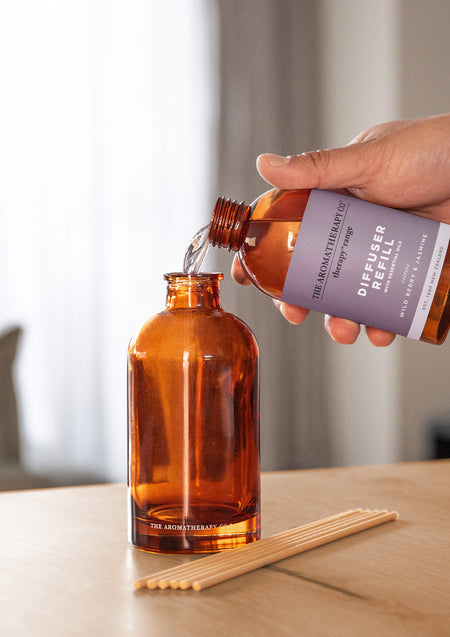 Hand refilling the Therapy amber diffuser bottle on a timber table