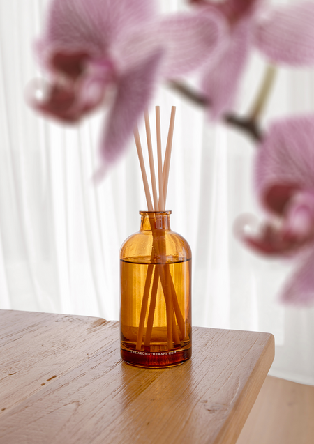 Therapy amber diffuser on timber with pink orchid blooms behind