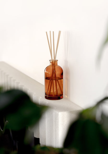 Therapy amber diffuser on a pale surface with a sheer curtain and green leaves