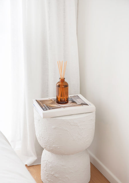 Therapy amber diffuser on a white pedestal beside a sheer curtain