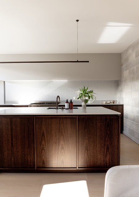 Dark timber kitchen seen from the living end, Therapy bottles and tulips on the island