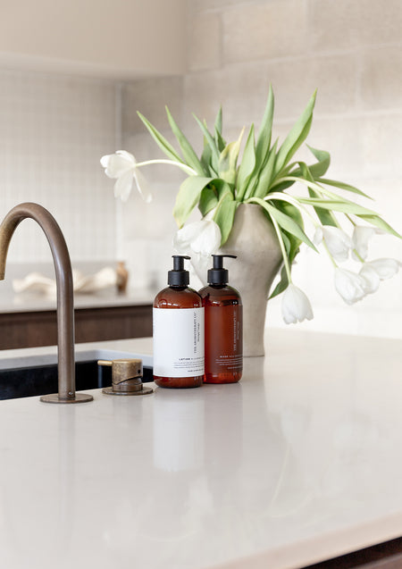 White tulips and amber Therapy bottles on a kitchen bench, brushed tap to one side