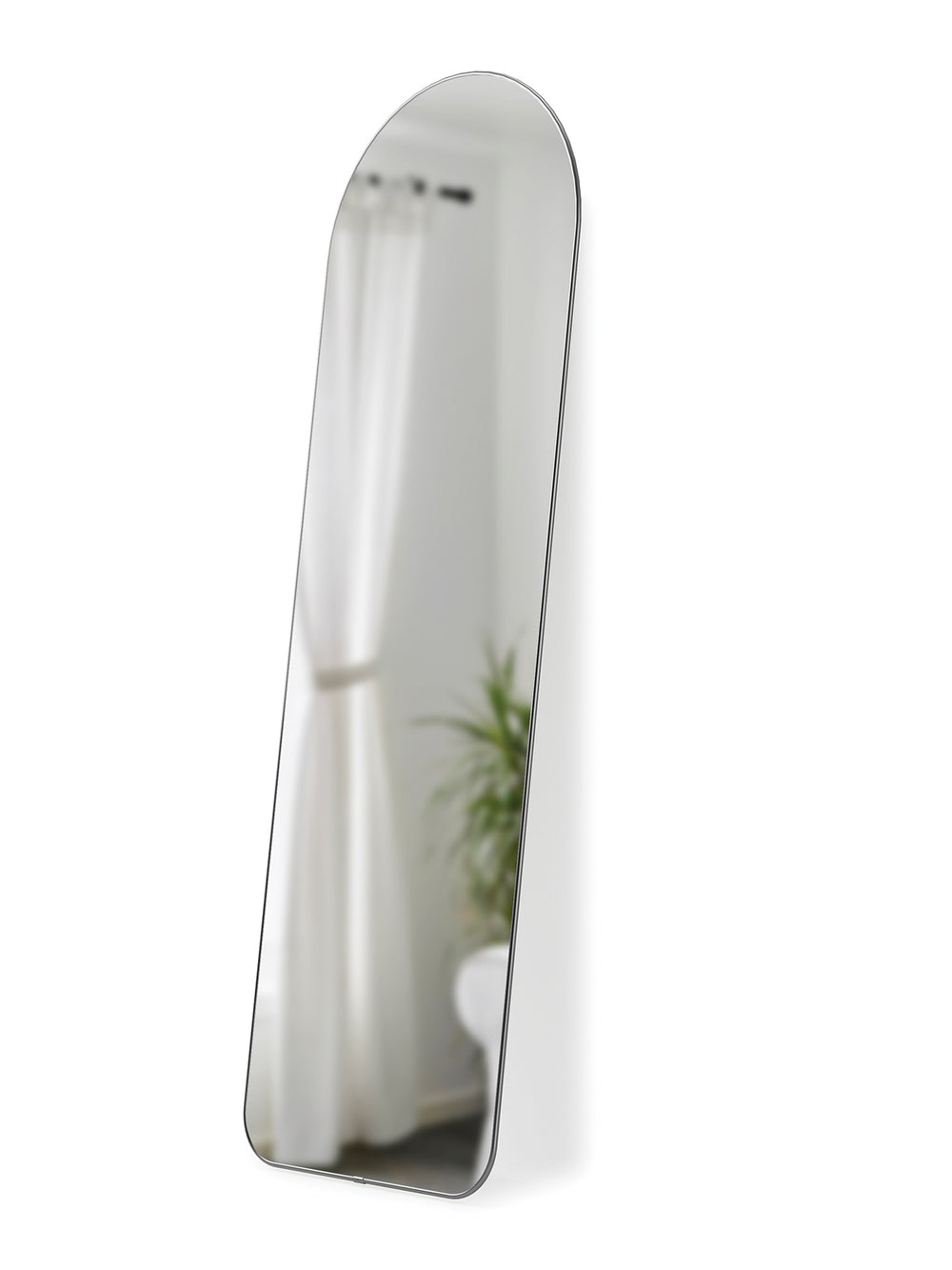 Umbra Hubba arched leaning mirror in titanium reflecting a curtained window and a plant