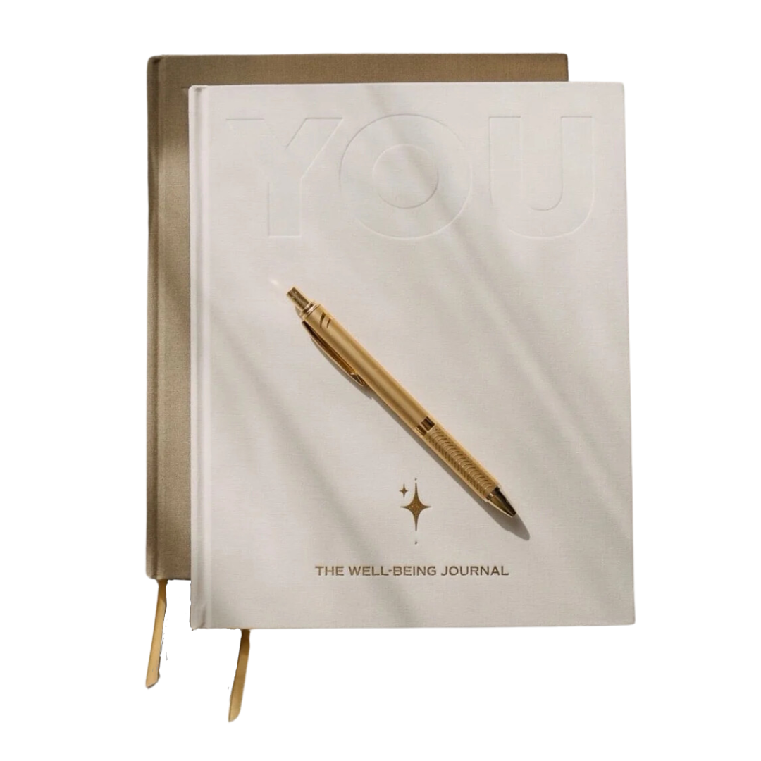 YOU. The Well-Being Journal in sand and cream, two copies stacked with a gold pen resting on the cover