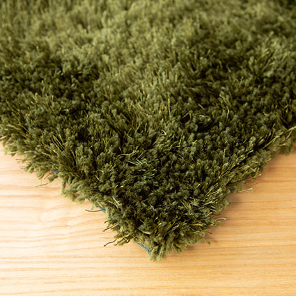 Corner of the olive green shaggy rug on a light timber floor