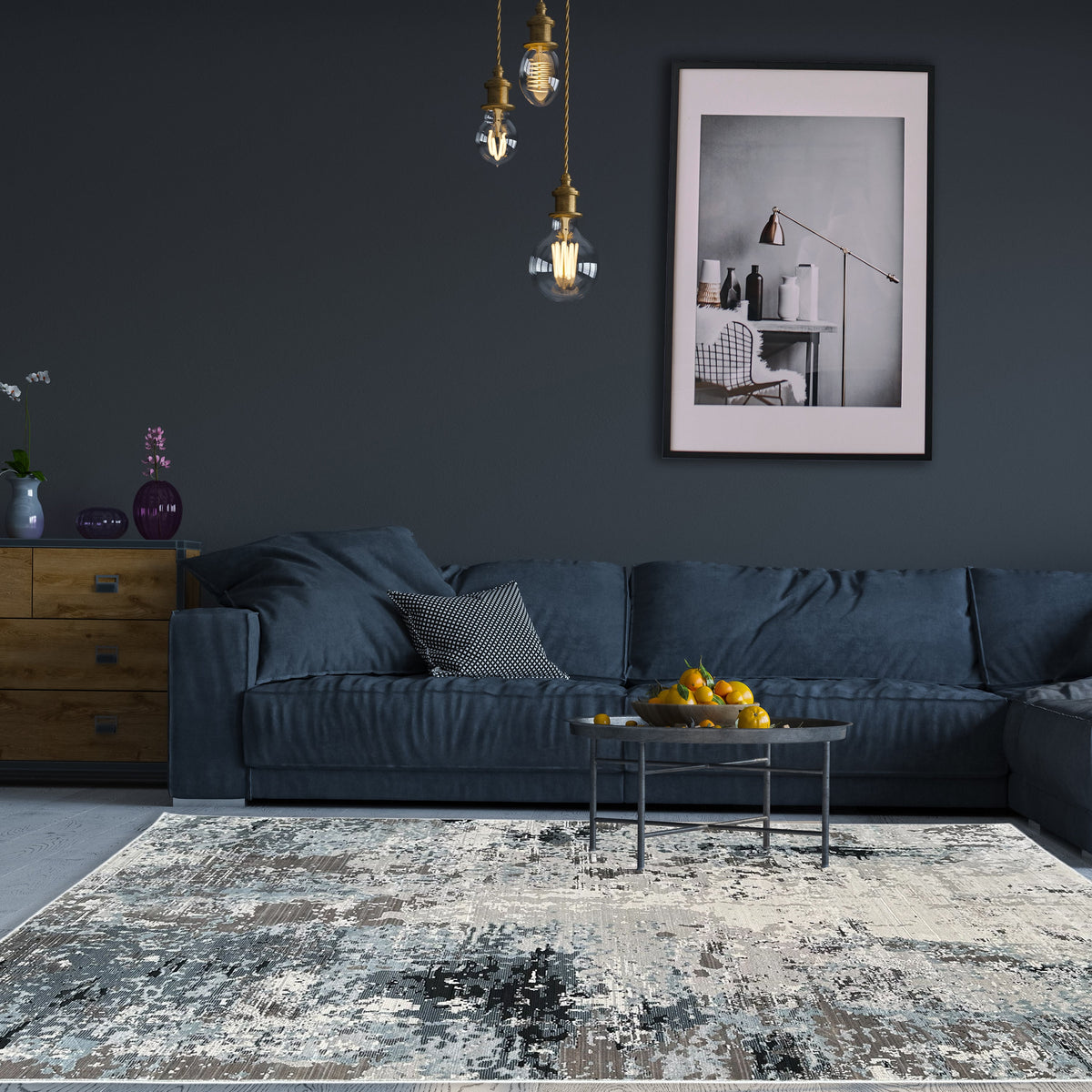 Grey abstract rug under a round metal coffee table in front of a slate sofa against a dark wall