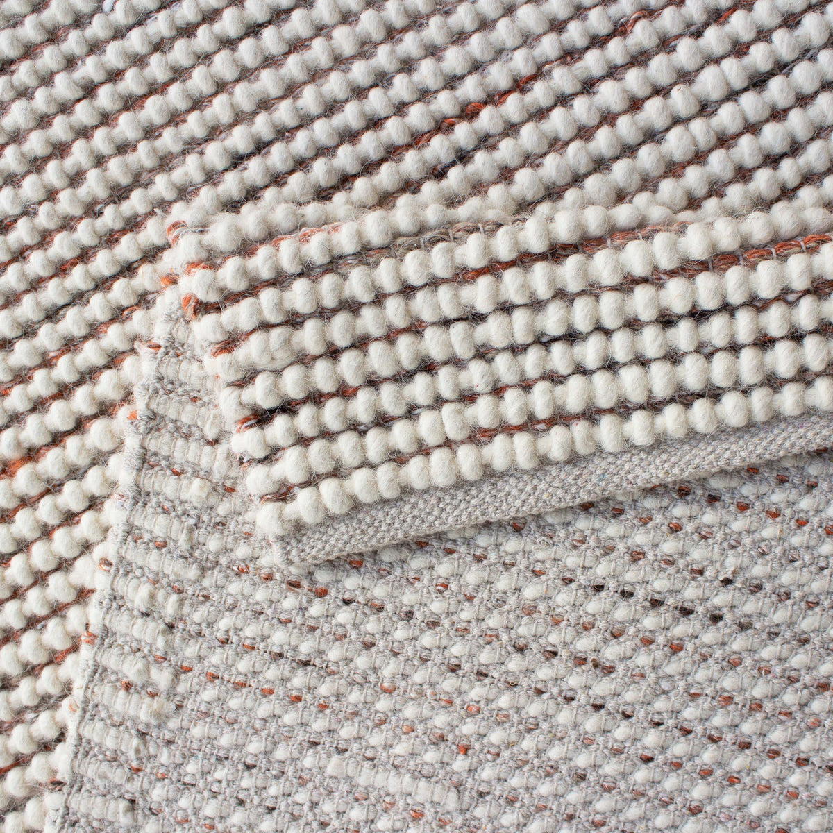 Folded corner of the ivory and rust knit rug showing the woven backing