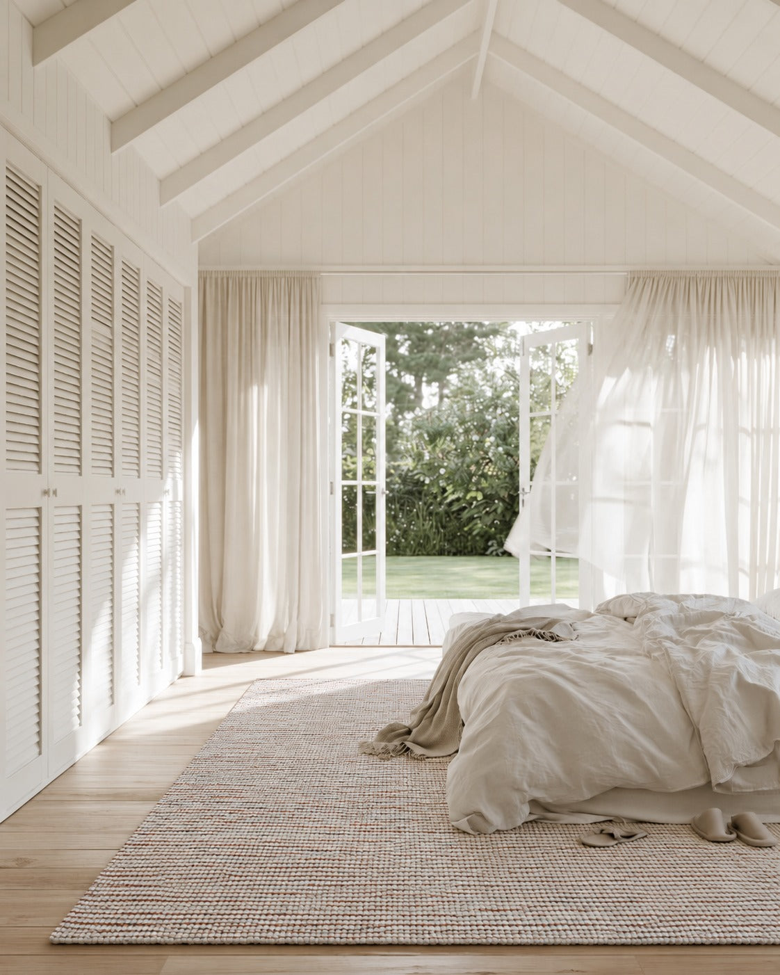 Aragon Wool Rust Rug under the end of a linen dressed bed in a white bedroom with louvre wardrobe doors
