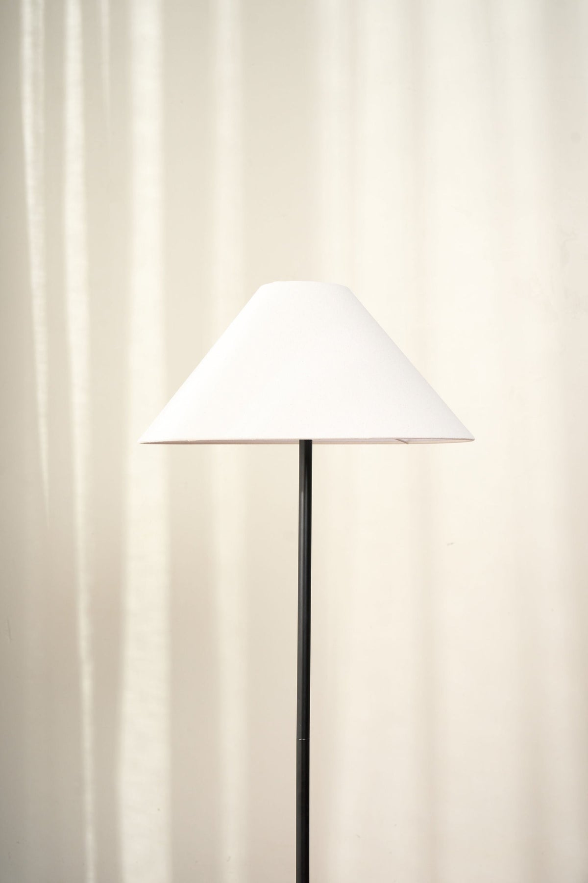 Close view of the cone-shaped linen shade on the fine black stem against a pale curtain