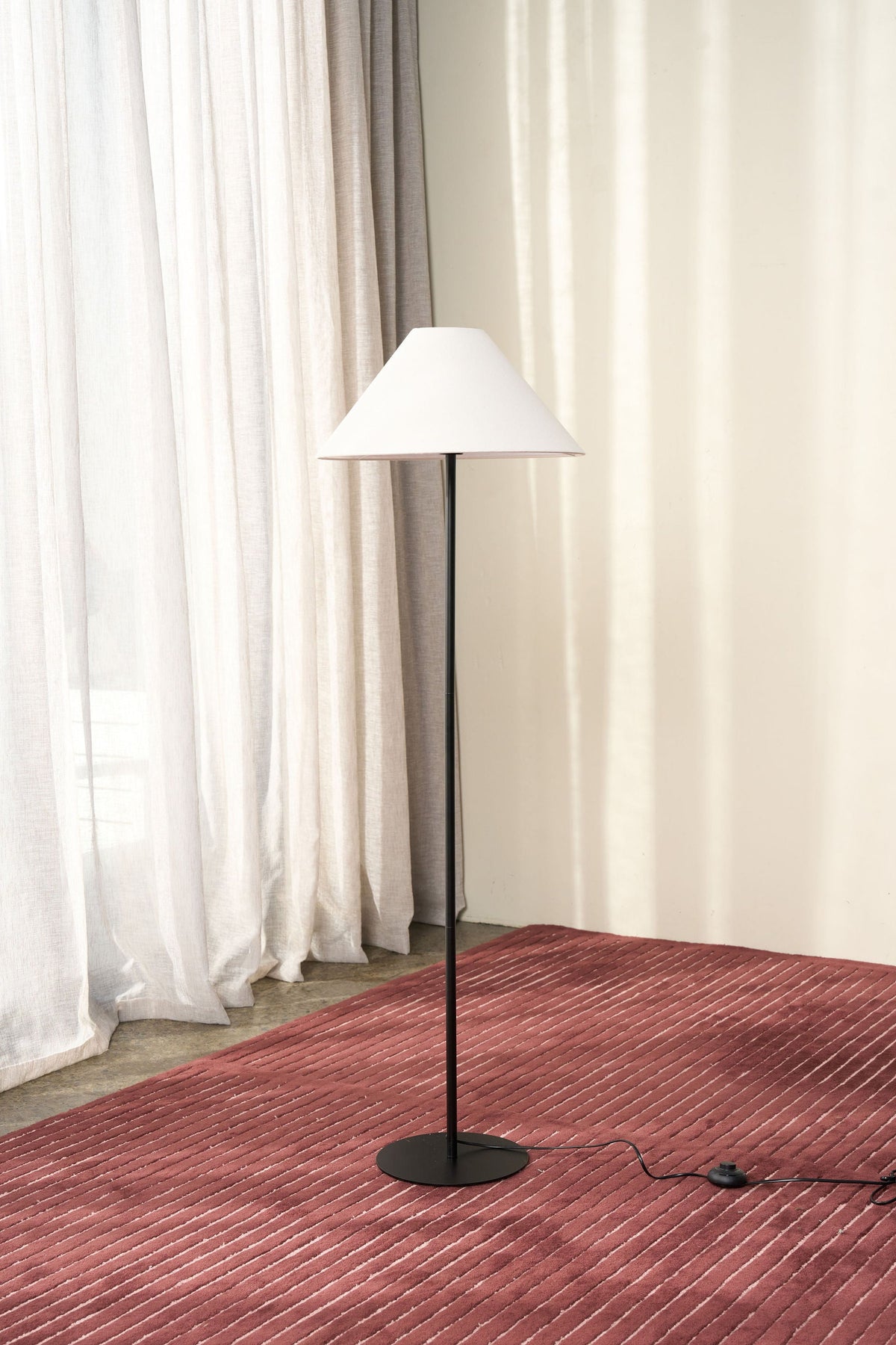 Arch Floor Lamp by Ned Collections, slim black stem and wide natural linen shade, on a rust rug by sheer curtains