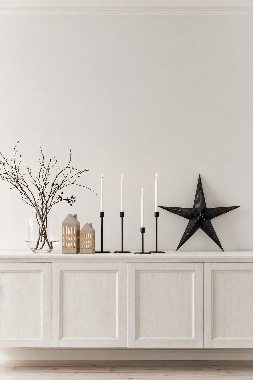 Two arrow window house tealight holders glowing on a white sideboard beside black candlesticks and a star