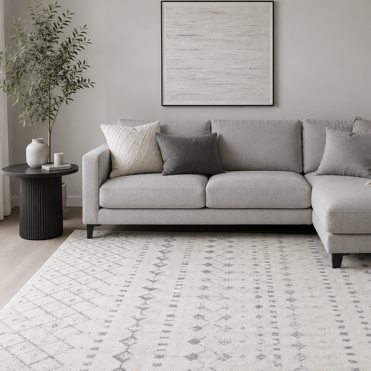Ivory and grey patterned rug in a living room with a grey sectional sofa, olive tree and framed artwork