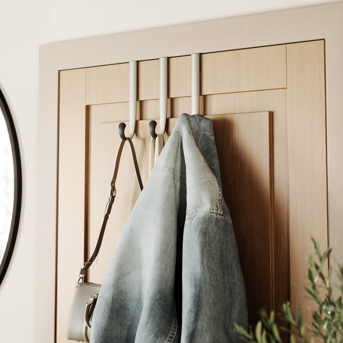 Umbra Schnook over-the-door hooks on a timber door holding a coat and a bag