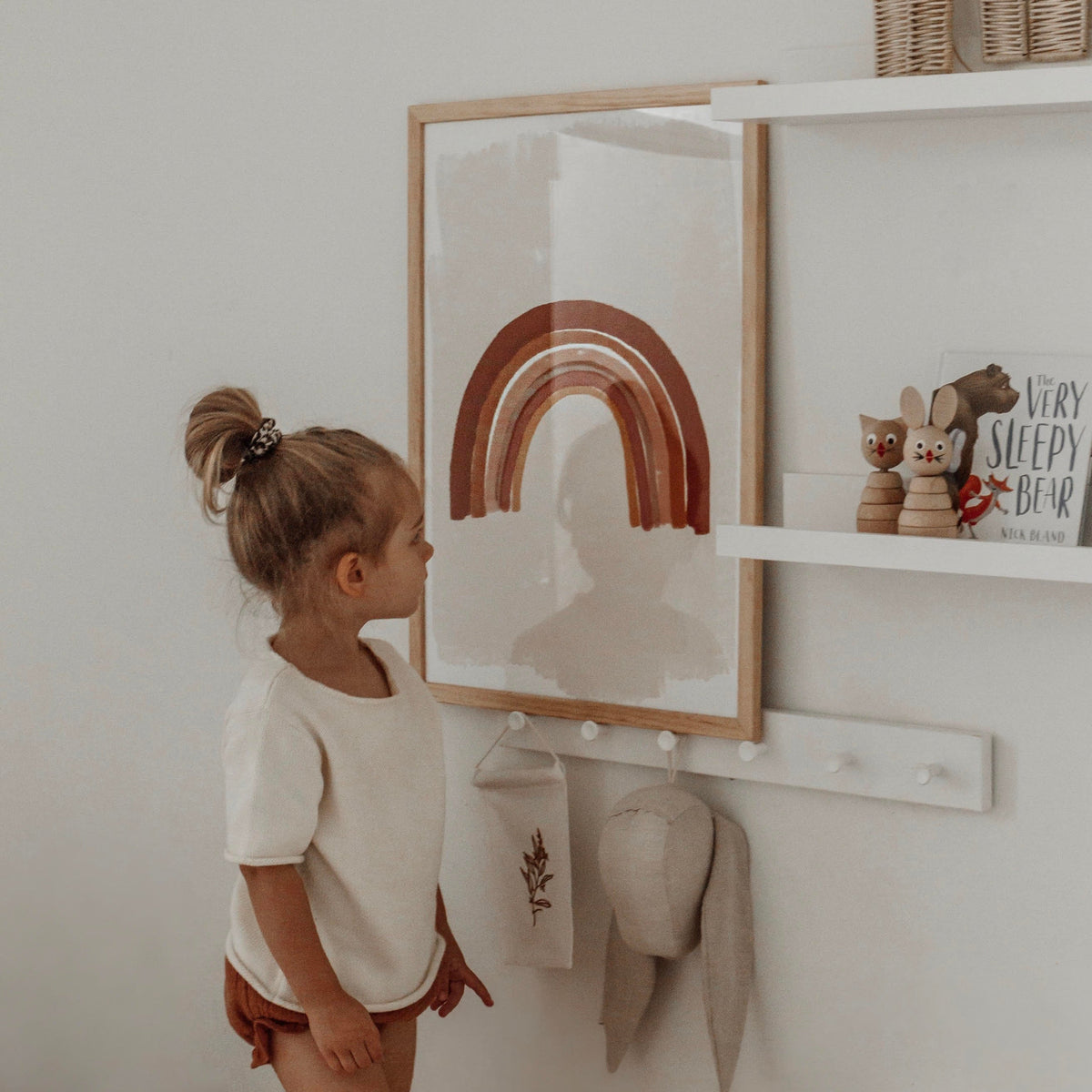 Toddler looking up at the Boho Rainbow print in a natural frame in a nursery