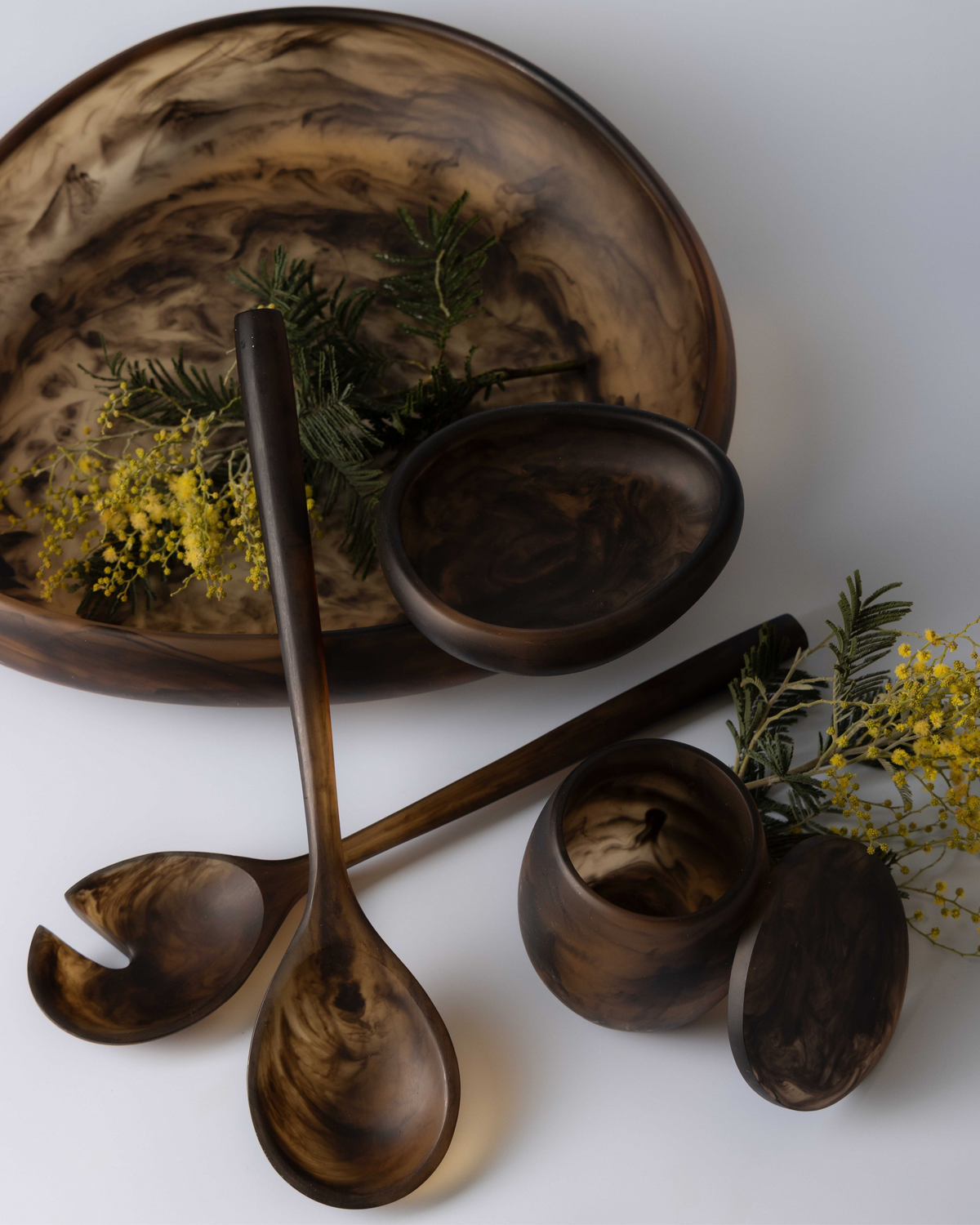 Chocolate small bowl inside a large resin bowl with salad servers, a tumbler and yellow wattle sprigs