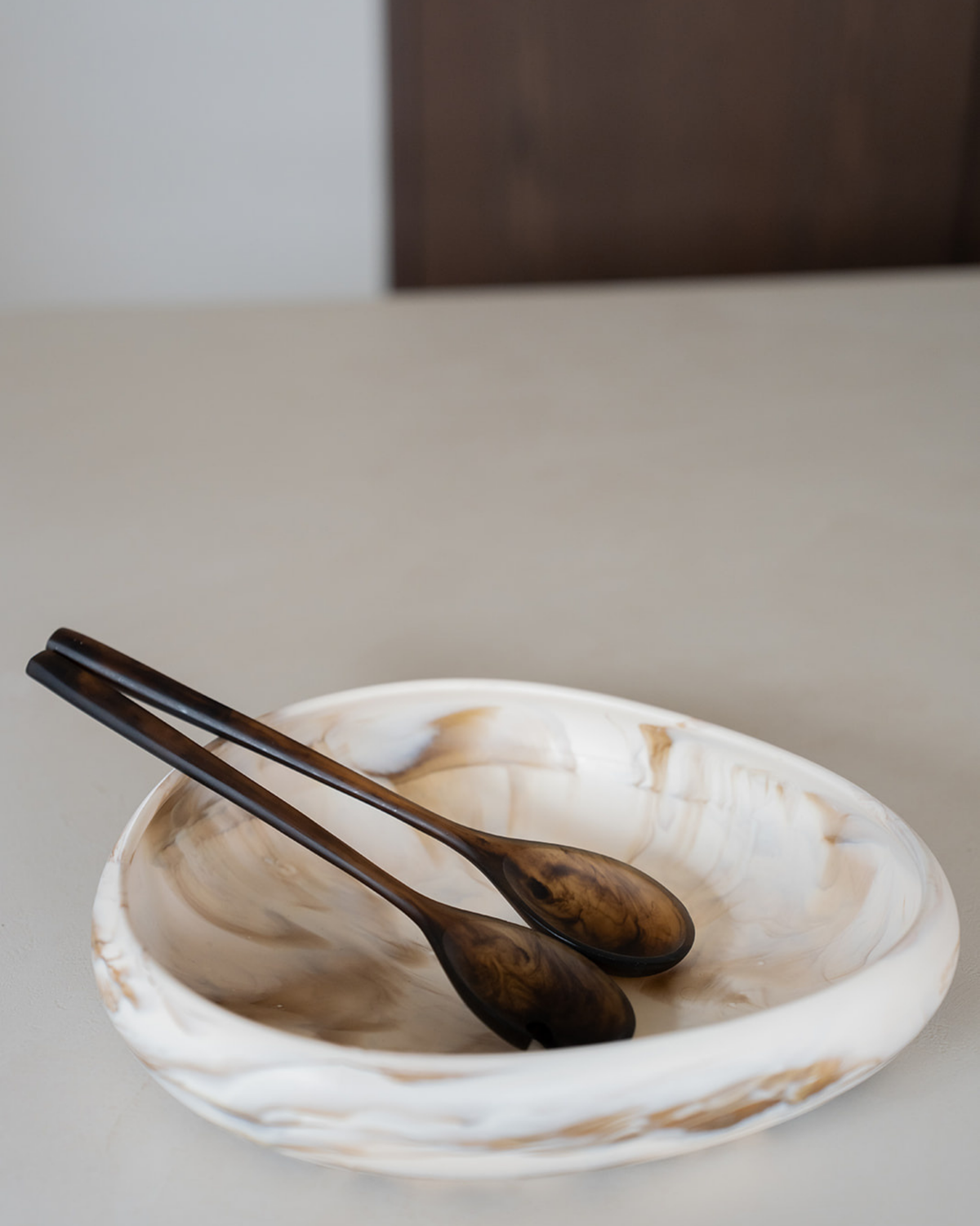 Chocolate salad servers resting in a large cream marbled resin bowl on a kitchen bench