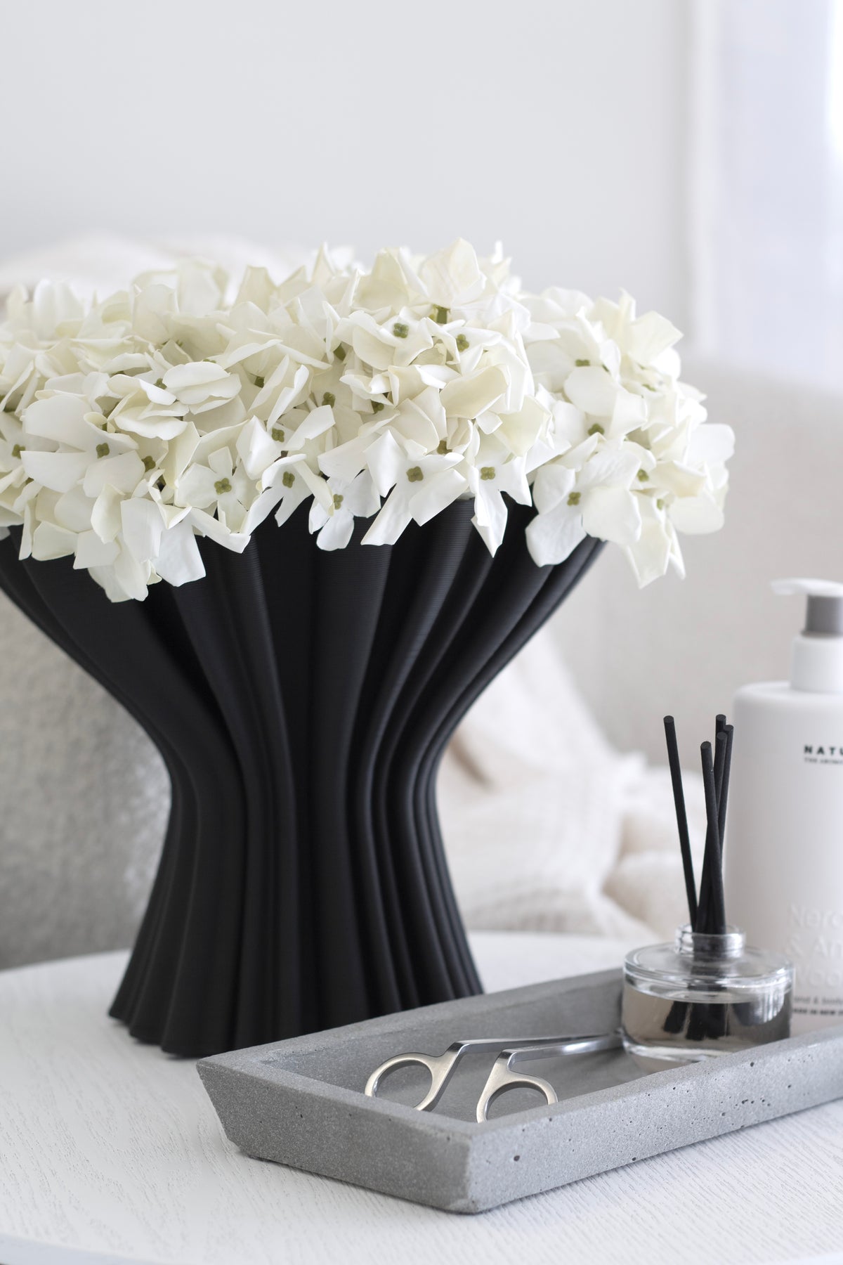 Black Cleo compote vase filled with white hydrangeas beside a stone tray