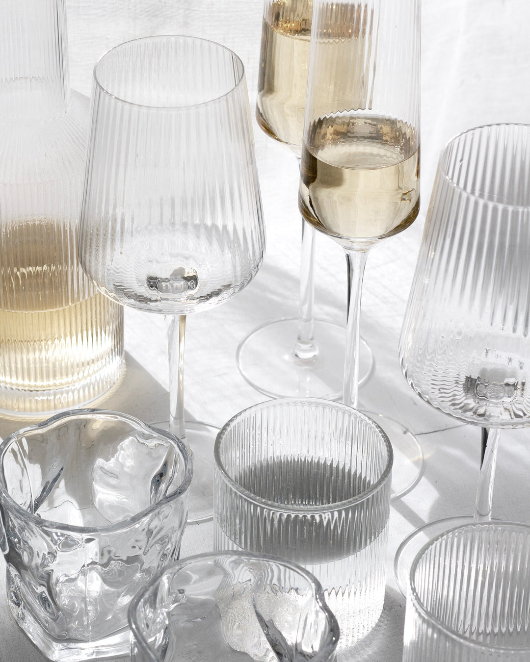Amalfi wine glasses and fluted tumblers arranged on a white table in sunlight