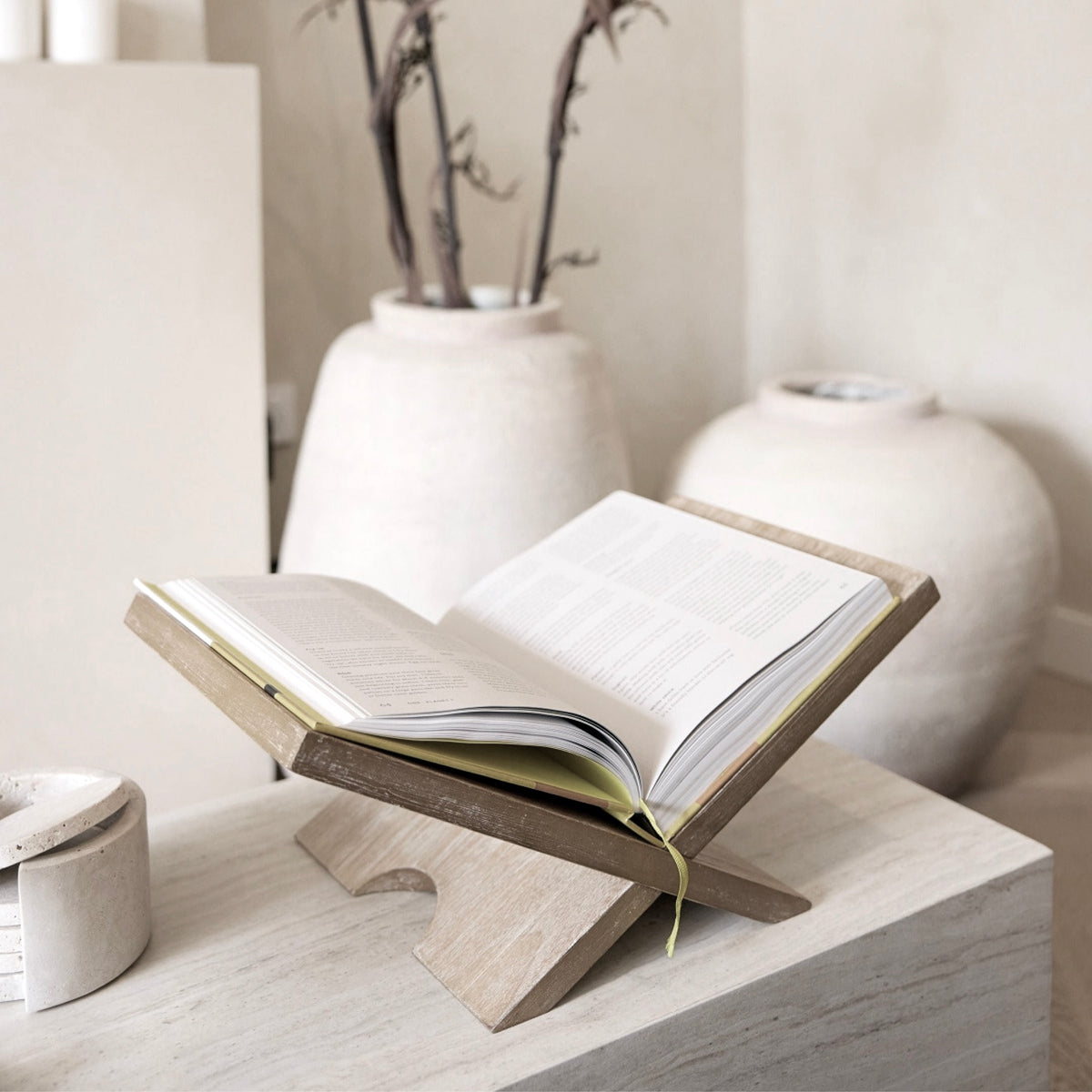 Natural Como book stand holding an open book beside cream ceramic vases