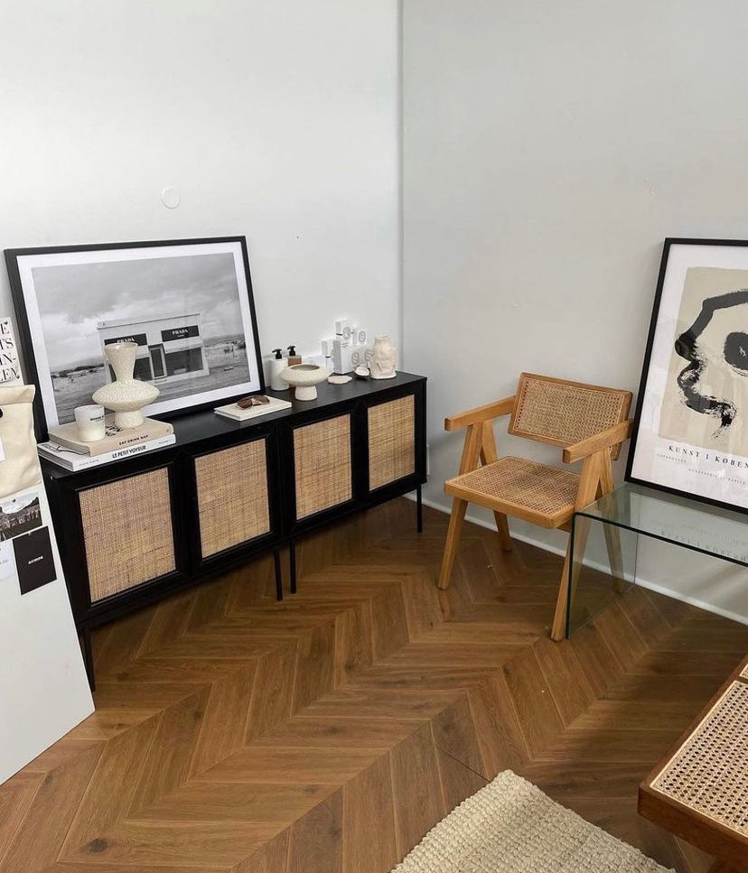 Copenhagen print framed in a corner beside a rattan chair and black sideboard on herringbone floors