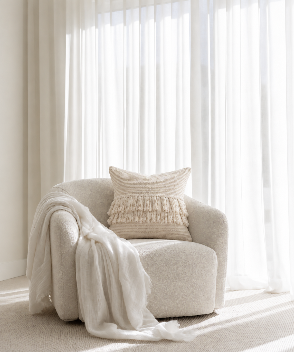 Cream Woven Cushion with handwoven fringe on a boucle armchair with a white throw beside sheer curtains
