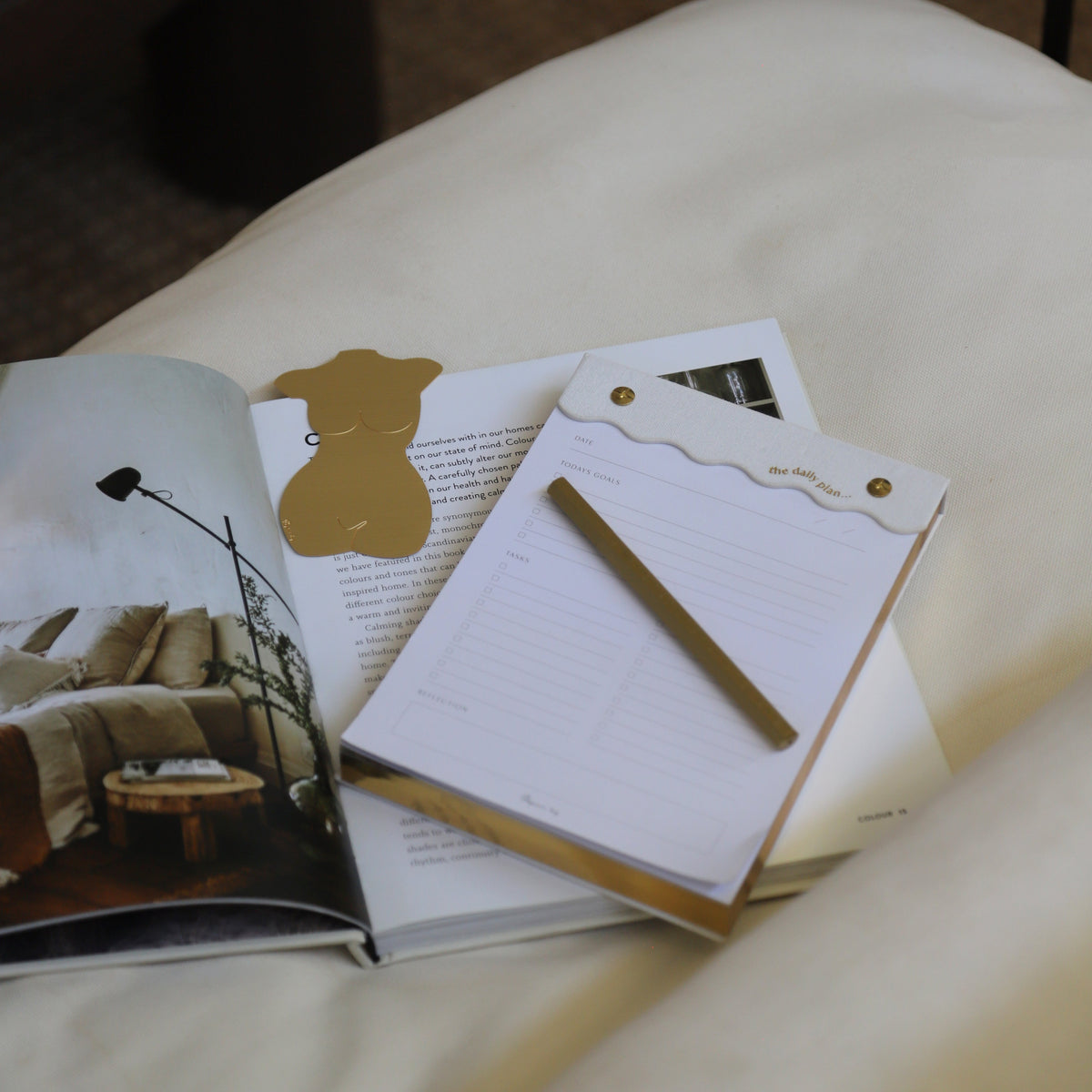 Curved daily notes pad on a bed with an open book, gold pen and glass
