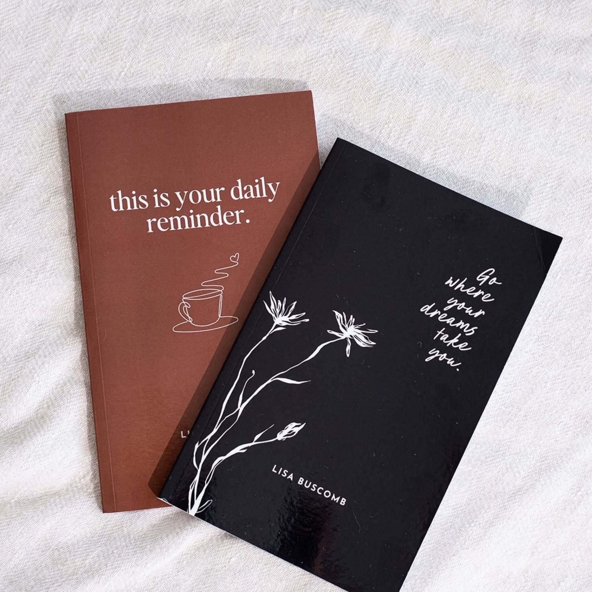 This Is Your Daily Reminder beside the black cover of Go Where Your Dreams Take You on a cream throw
