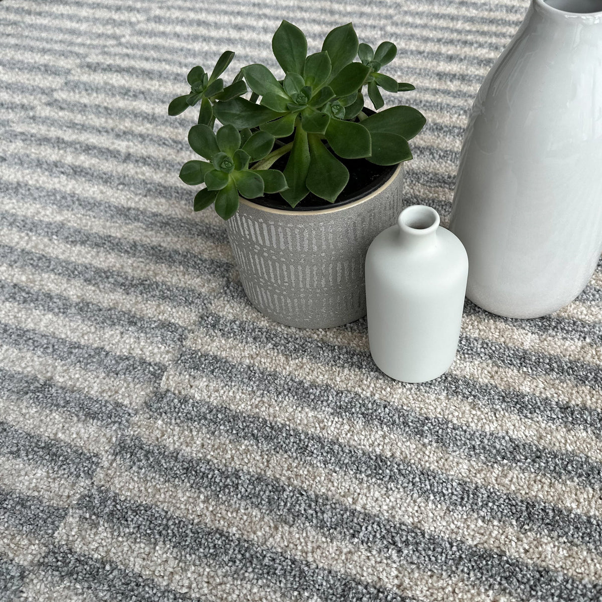 Cream and dark grey stripe pile with a potted succulent and white ceramic vases on top