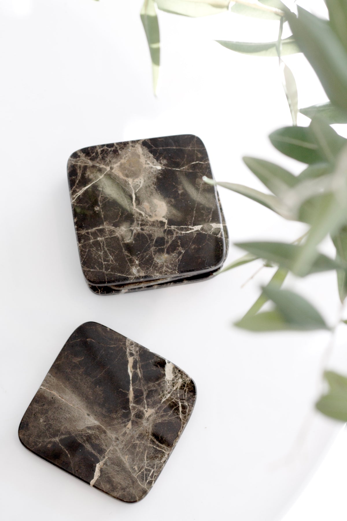 Dark marble and travertine stone coasters styled on white surface with natural light, modern table décor