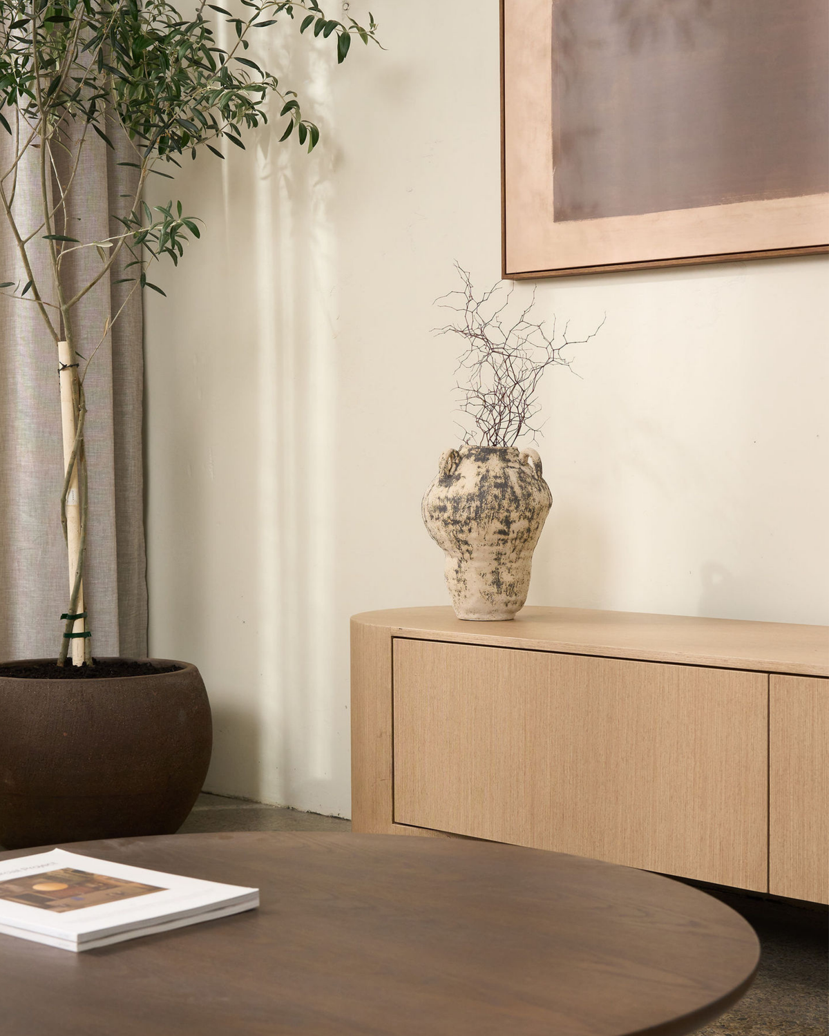 Large vase with dried branches on a pale oak sideboard next to a potted olive tree