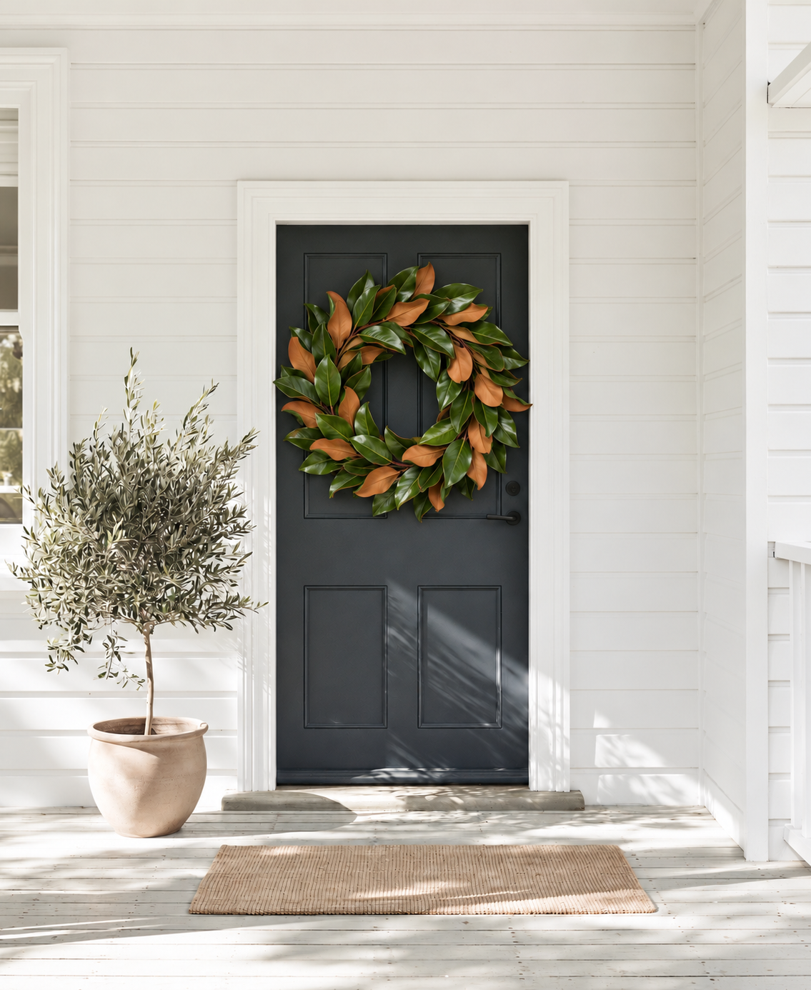Magnolia Leaf Wreath on a dark front door of a white weatherboard home beside a potted olive tree