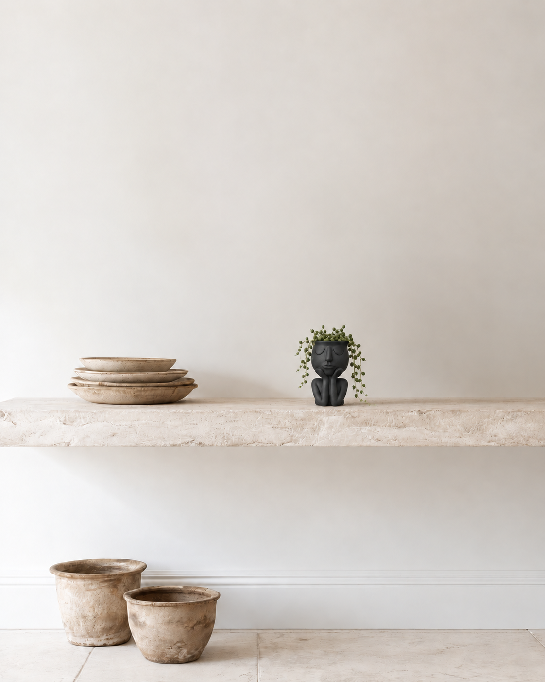 Dreamy Head Planter 15cm in black with trailing string of pearls on a stone shelf beside stacked plates