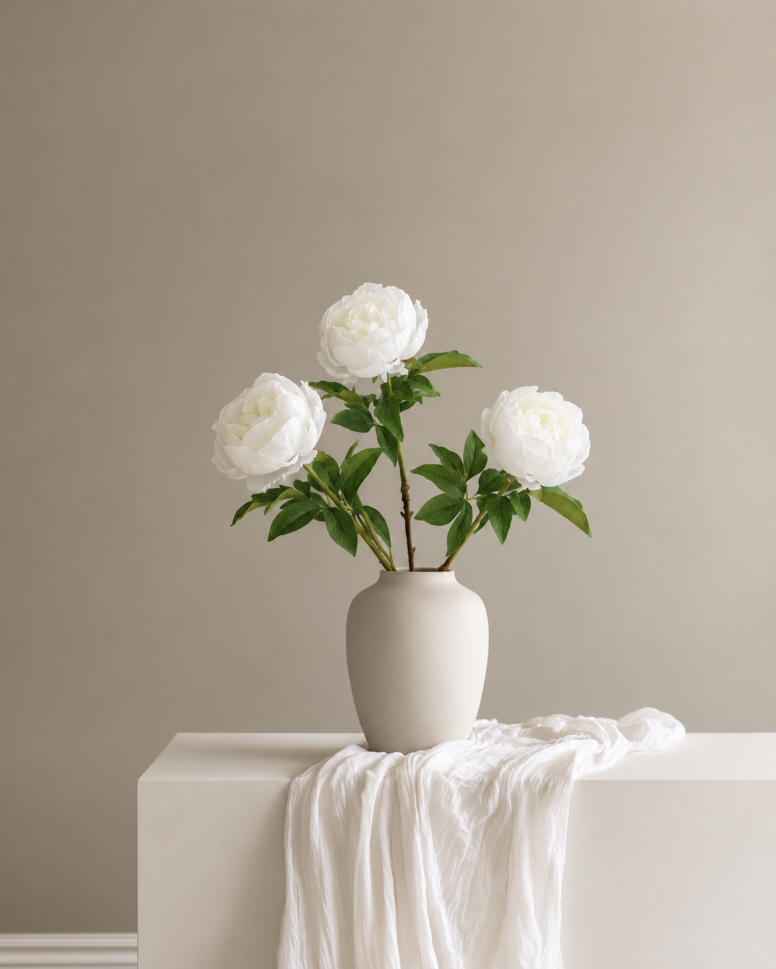 Duchess Peony Stems in white in a stone ceramic vase on a console with soft linen