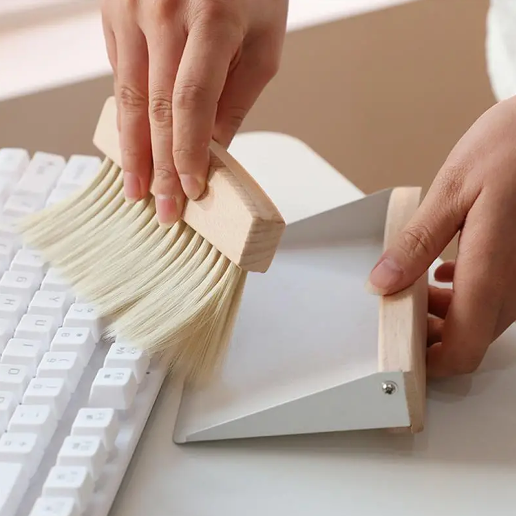 Sweeping debris off a white keyboard into the cream dustpan held alongside
