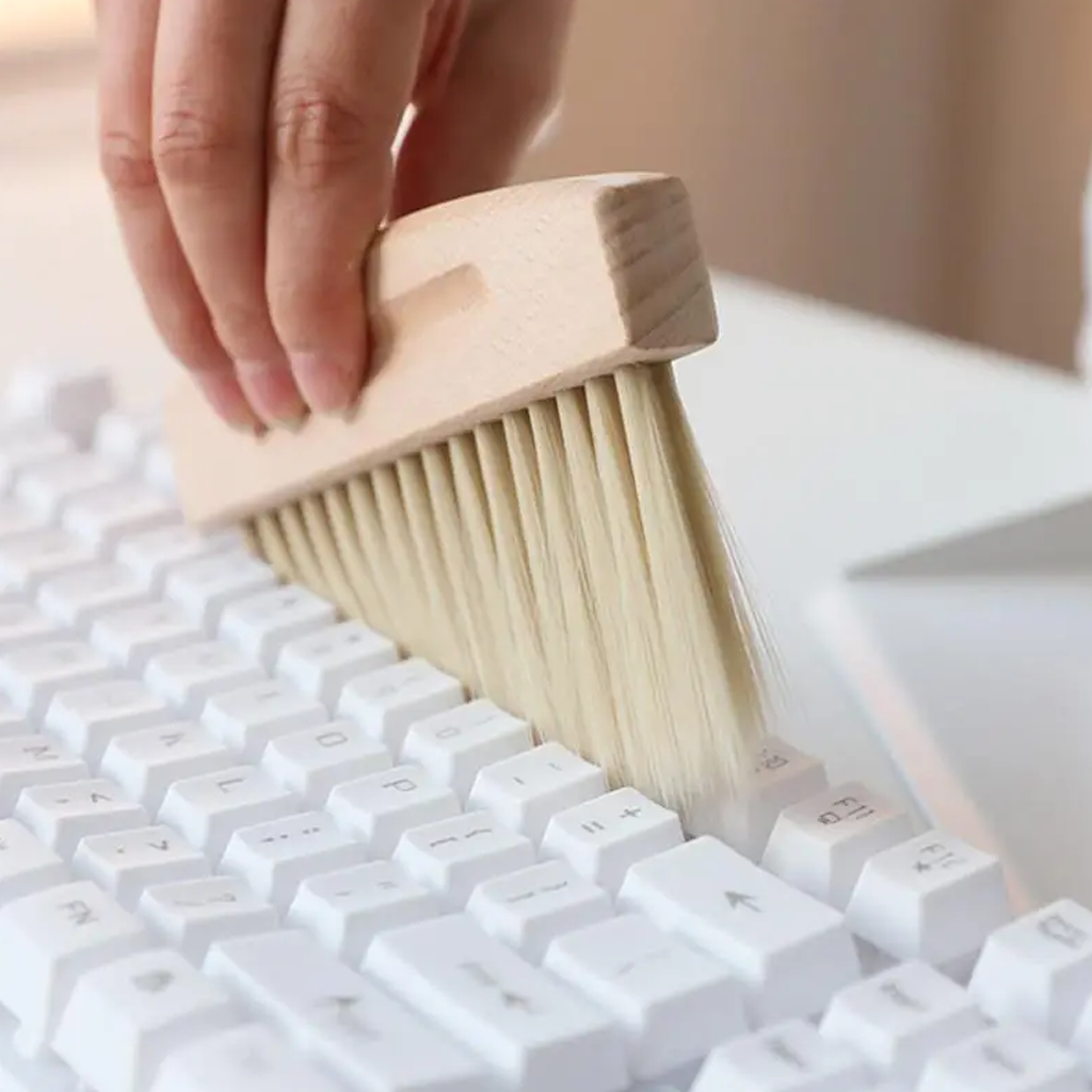 Brushing crumbs from between the keys of a white keyboard with the wooden handled brush