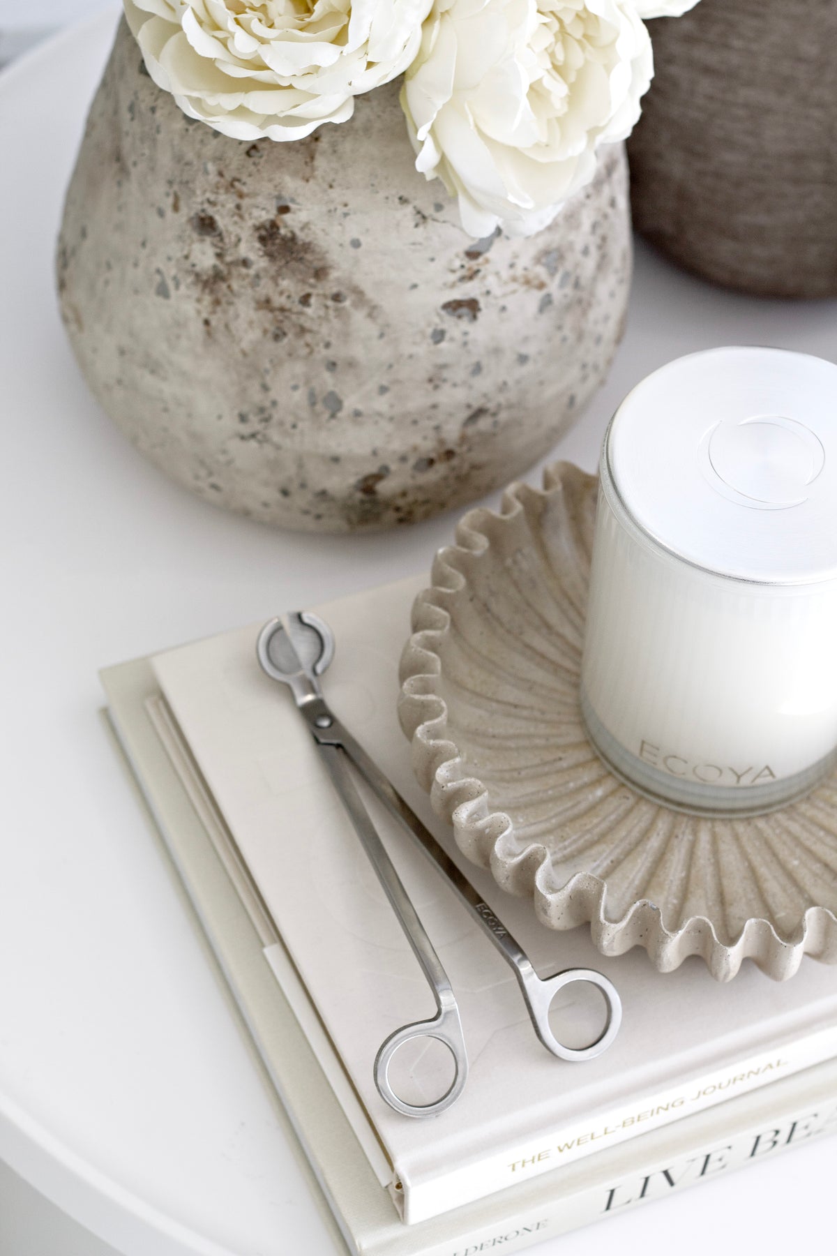 Ecoya stainless steel wick trimmer styled with candle and books on neutral coffee table.