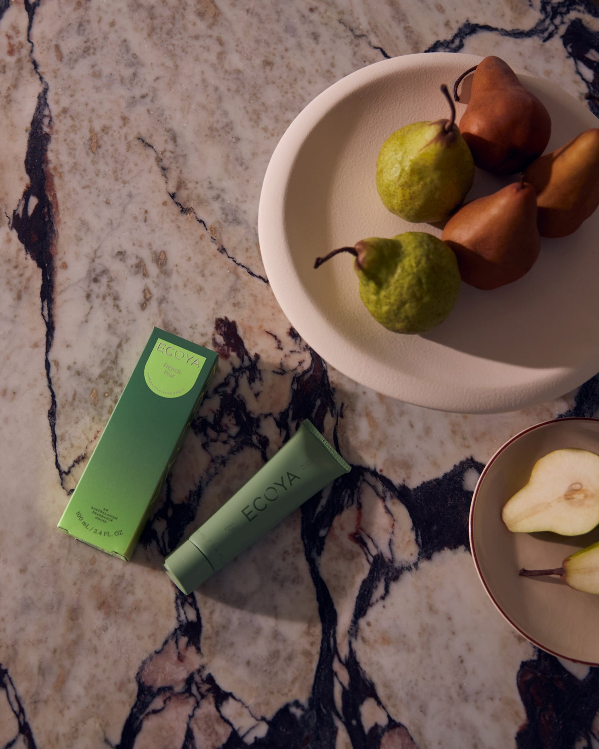 Green Ecoya hand cream with pears on a pink marble surface, overhead view