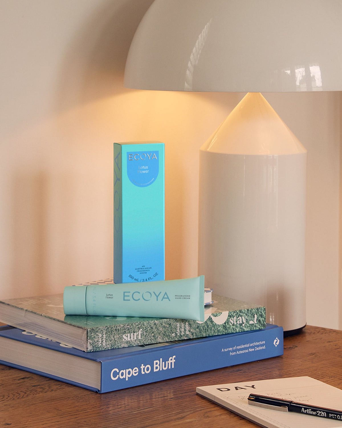 Teal Ecoya hand cream box on stacked books beside a glowing lamp