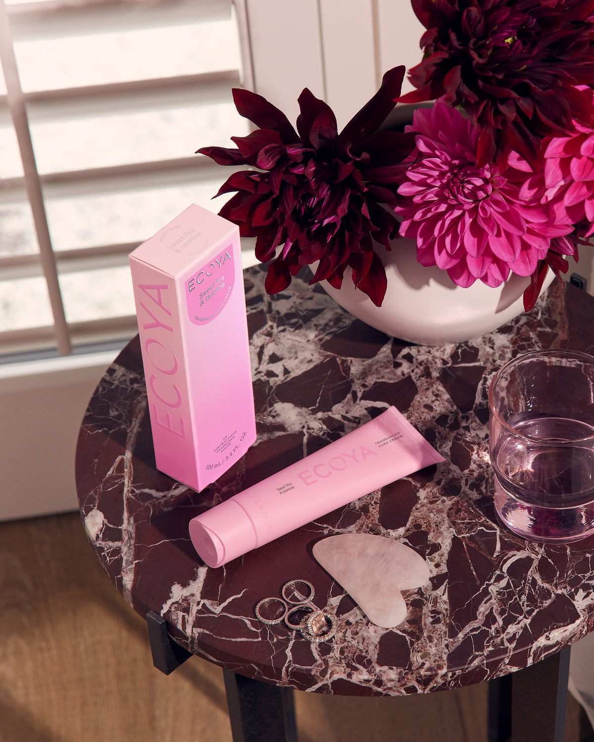 Pink Ecoya hand cream and box on a marble side table beside deep pink dahlias
