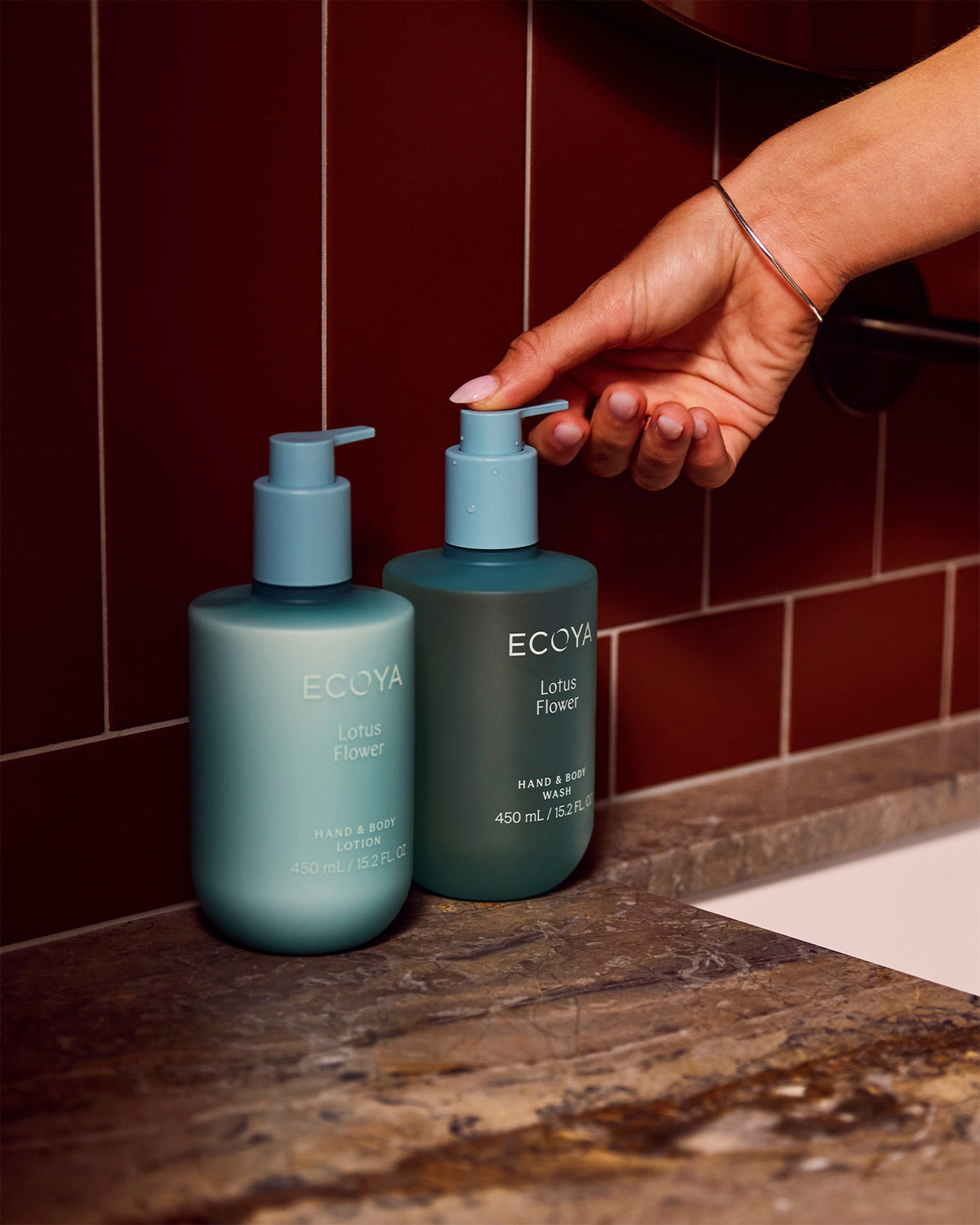 Ecoya Lotus Flower Hand & Body Wash and lotion in green on a marble vanity against deep red tiles
