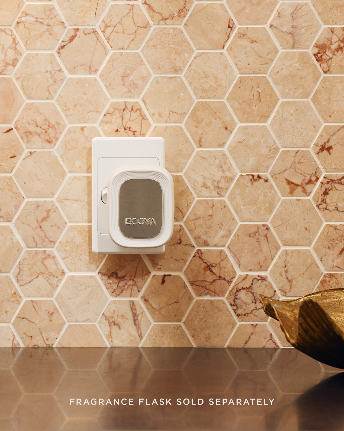 Ecoya Plug-In Diffuser in a white socket against a hexagonal marble tile splashback, beside a gold bowl